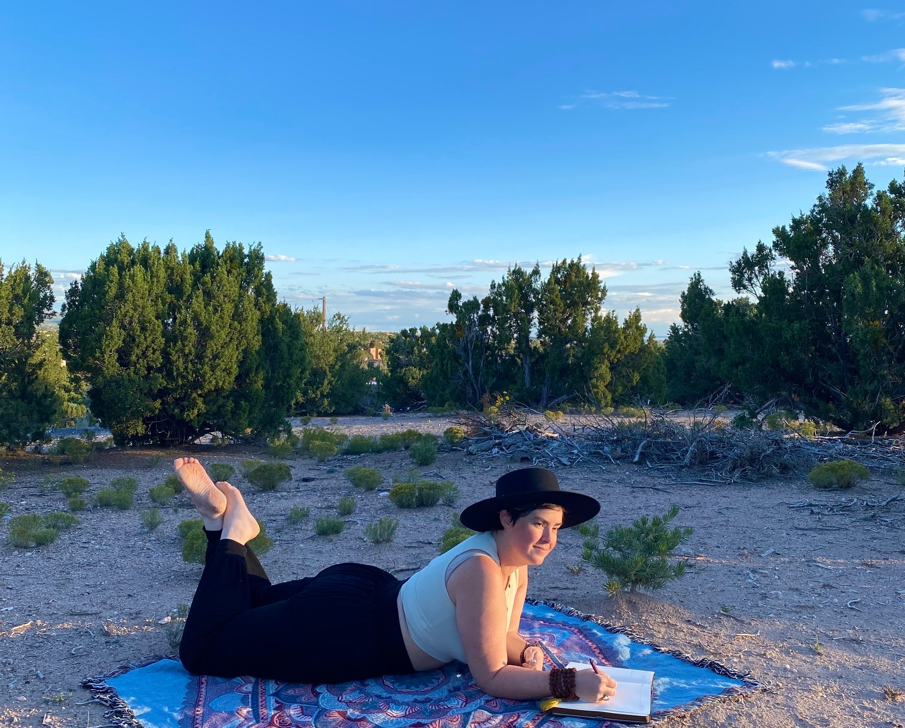 Mackenzie is on a ritual blanket in the desert, writing in a journal.