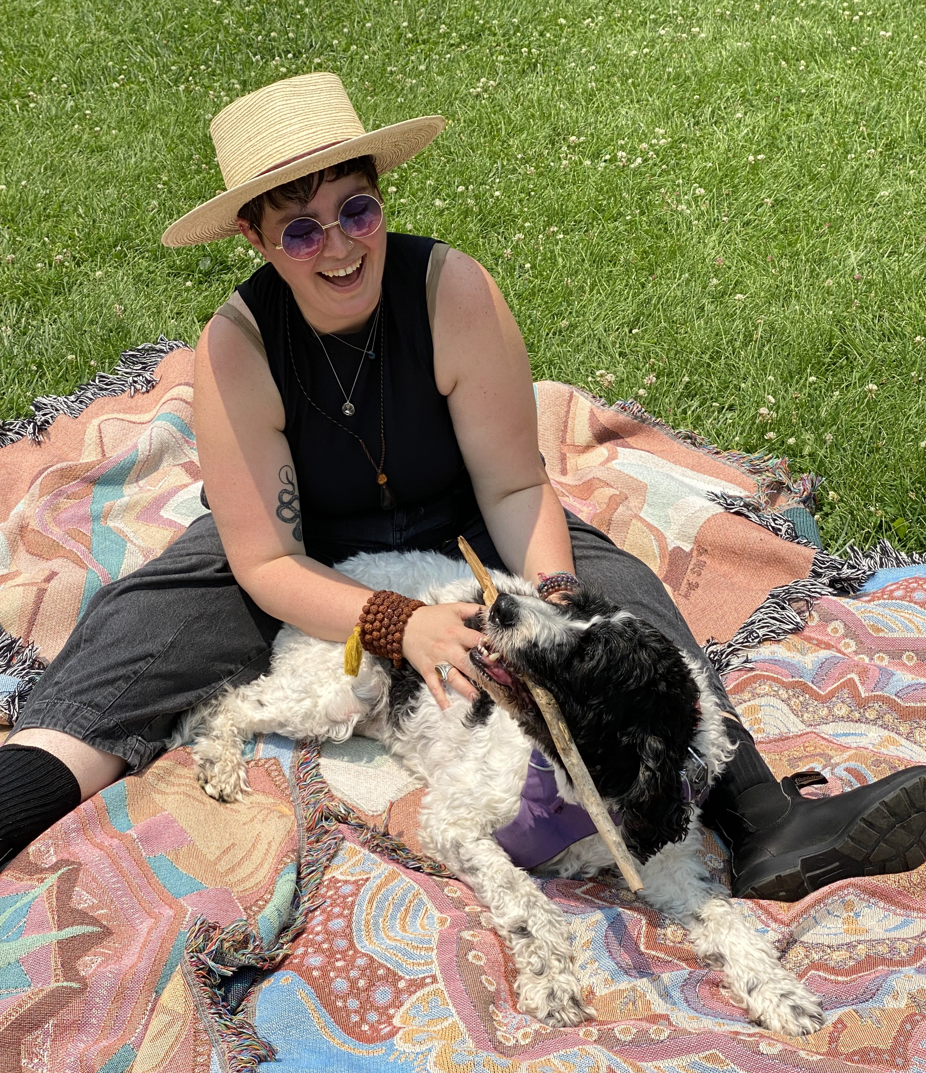 Mackenzie smiles while playing Peaches the dog on ritual blankets in the grass.