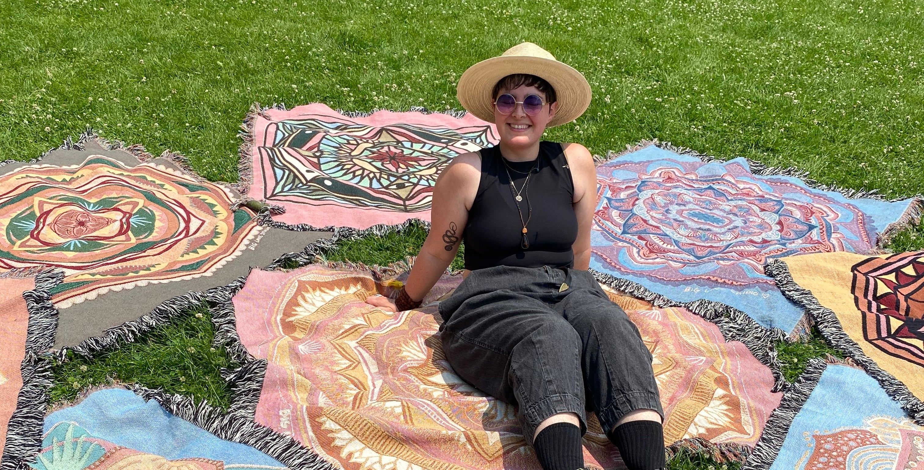 Mackenzie sits amongst bright ritual blankets on the grass.