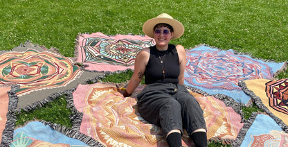 Mackenzie sits amongst bright ritual blankets on the grass.