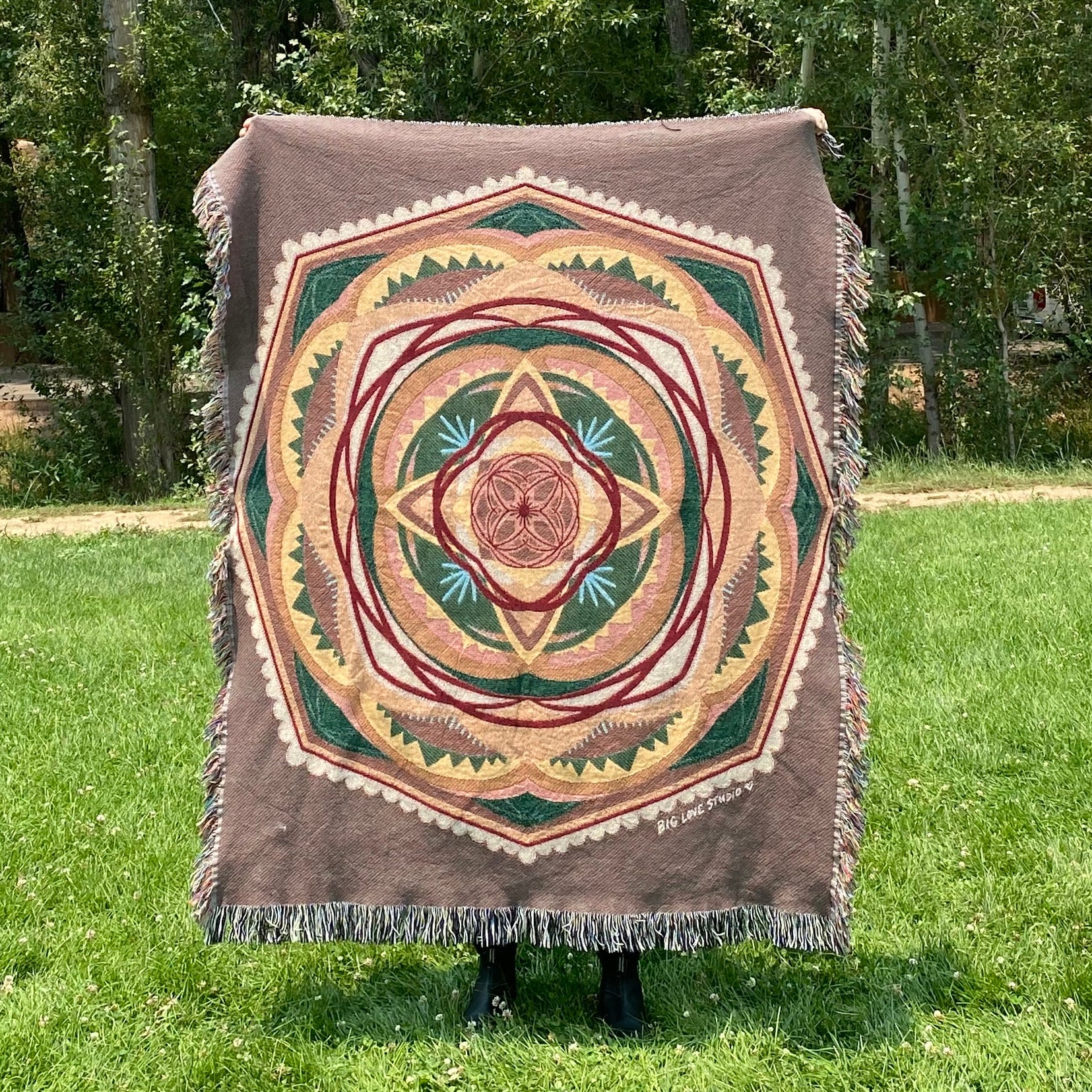 A colorful mandala woven blanket with fringe in browns, greens, and yellows