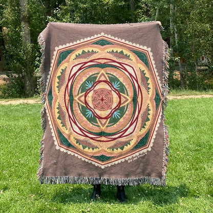 A colorful mandala woven blanket with fringe in browns, greens, and yellows