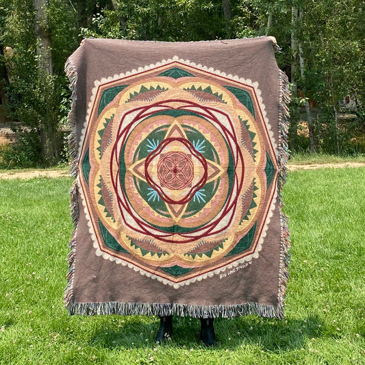 A colorful mandala woven blanket with fringe in browns, greens, and yellows
