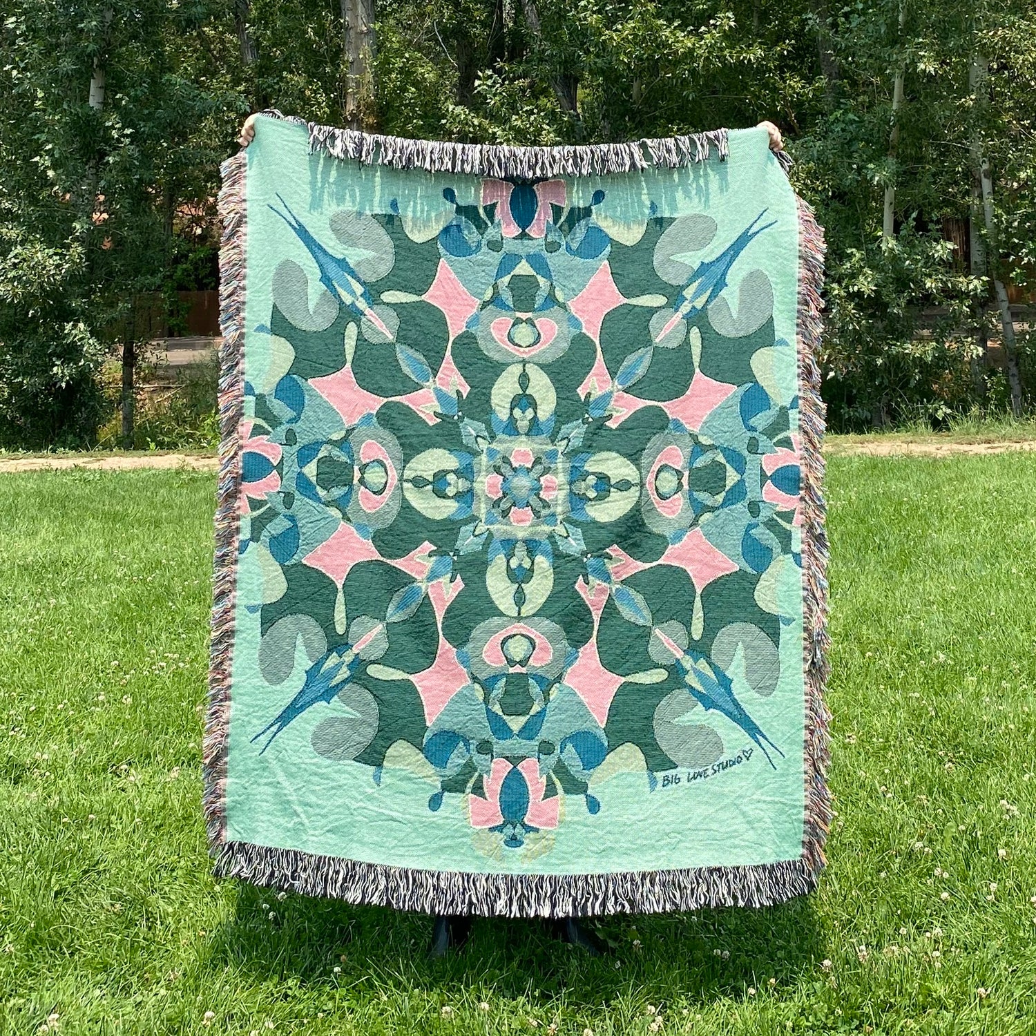 A colorful patterned kaleidoscope blanket with fringe in main colors of light and dark greens