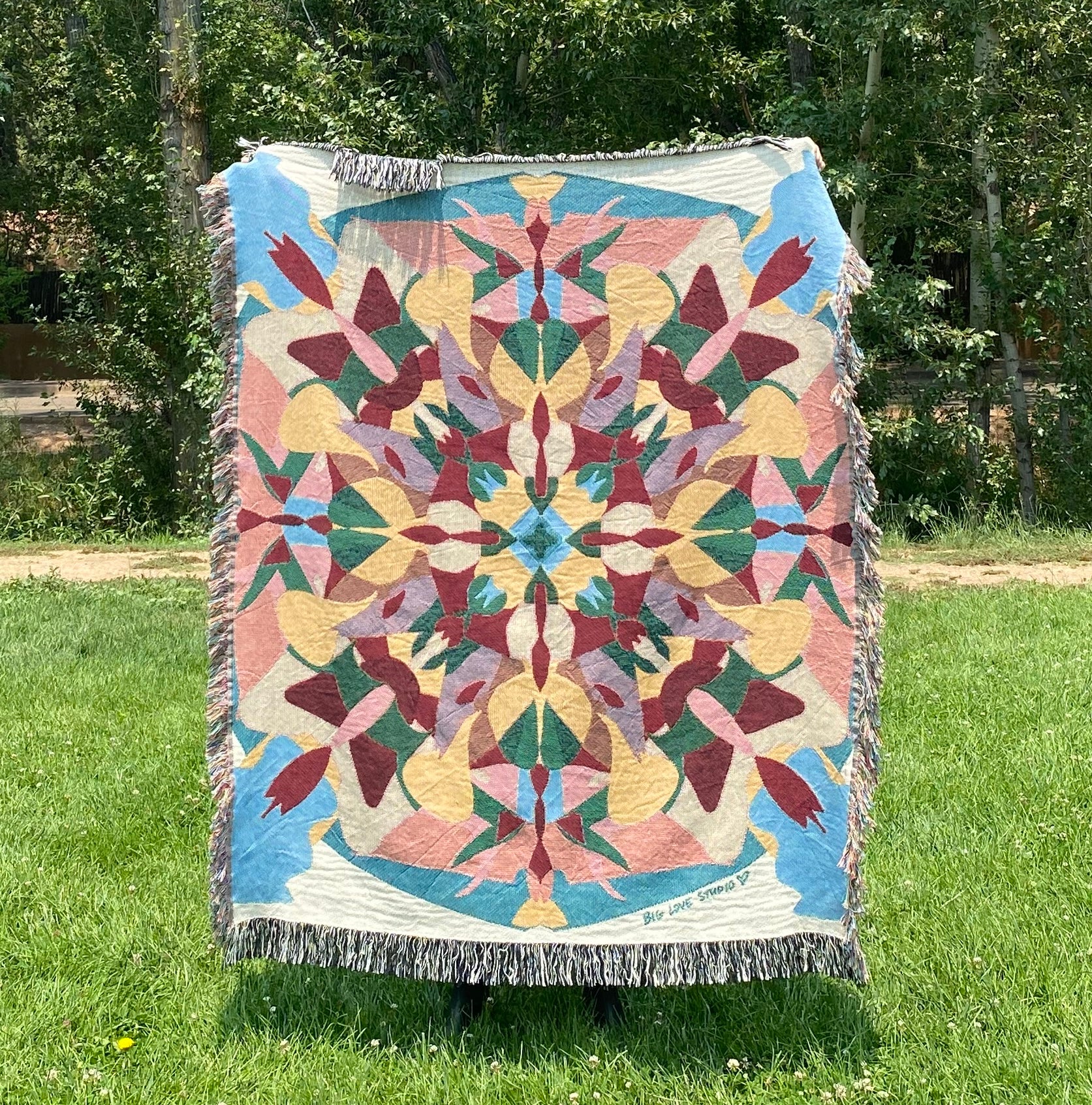A colorful patterned kaleidoscope blanket in blues, pink, yellow, red, and green with fringe