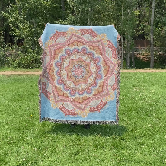 Mackenzie flips a brightly colored mandala woven blanket with fringe to see the front and back
