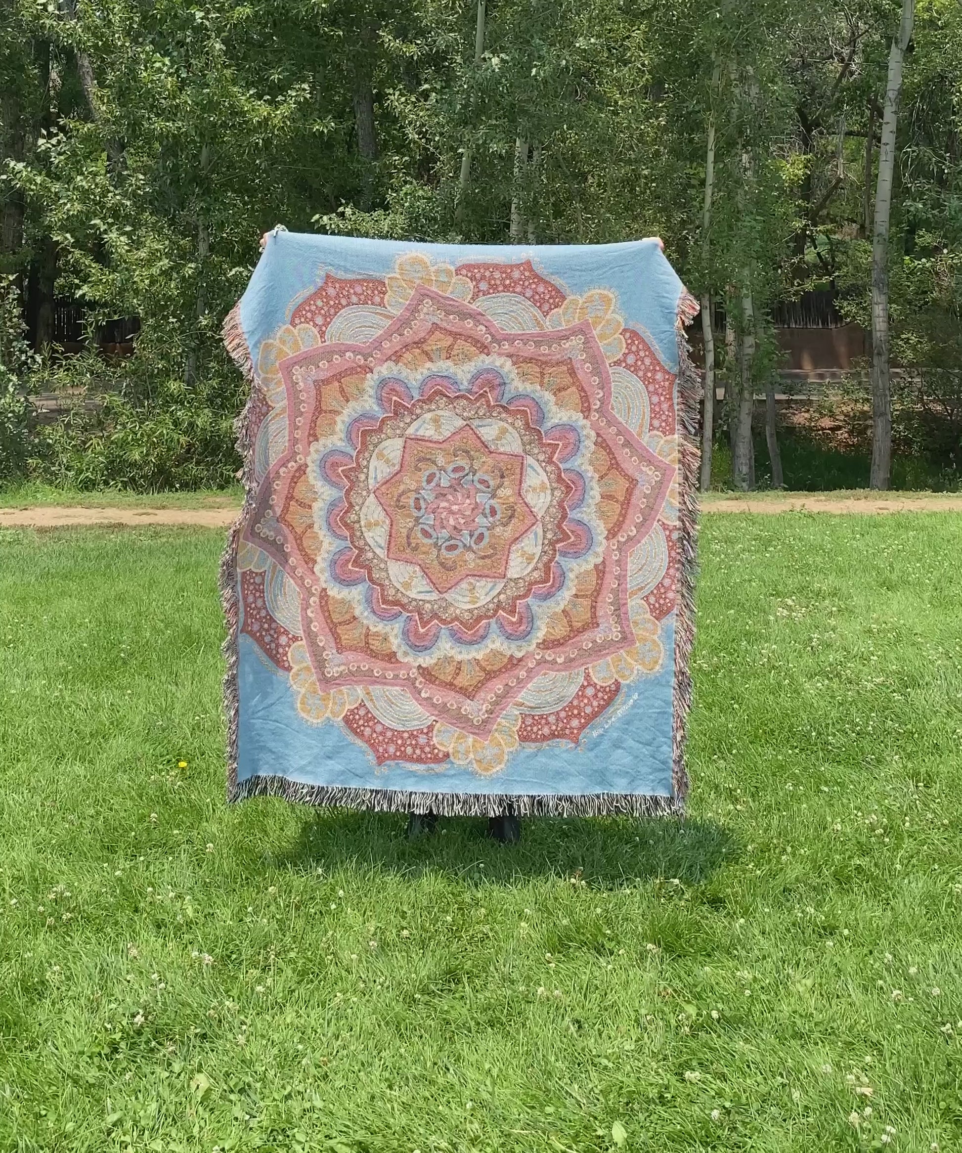 Mackenzie flips a brightly colored mandala woven blanket with fringe to see the front and back