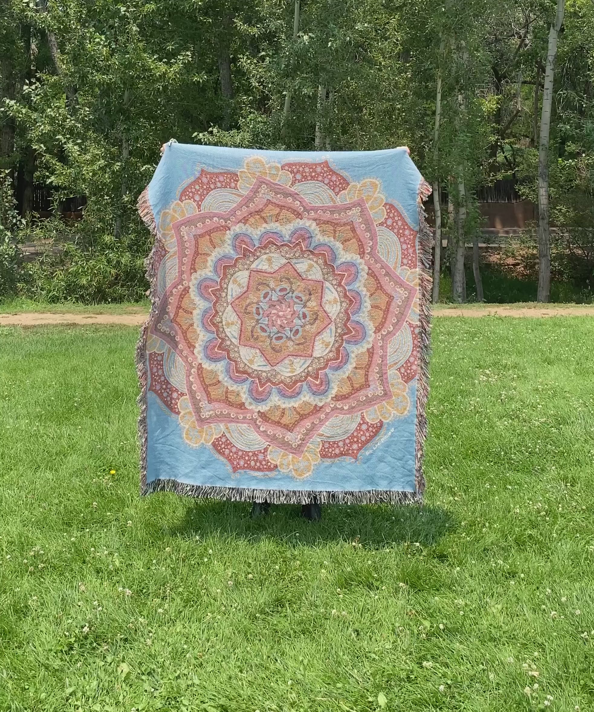 Mackenzie flips a brightly colored mandala woven blanket with fringe to see the front and back