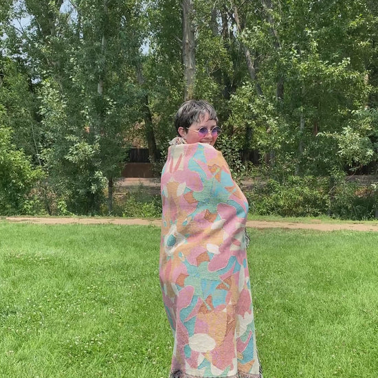Video of Mackenzie wrapped in a colorful patterned kaleidoscope patterned blanket with fringe