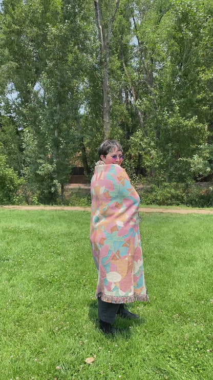 Video of Mackenzie wrapped in a colorful patterned kaleidoscope patterned blanket with fringe