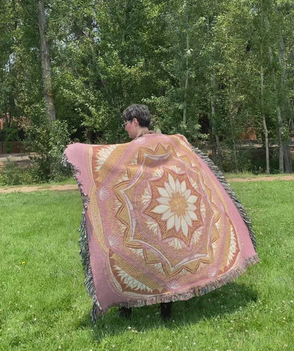 Mackenzie flips a pink and golden mandala woven blanket with fringe to see the front and back