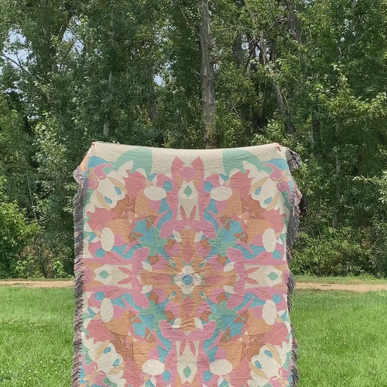 Mackenzie flips a brightly colored kaleidoscope woven blanket with fringe to see the front and black