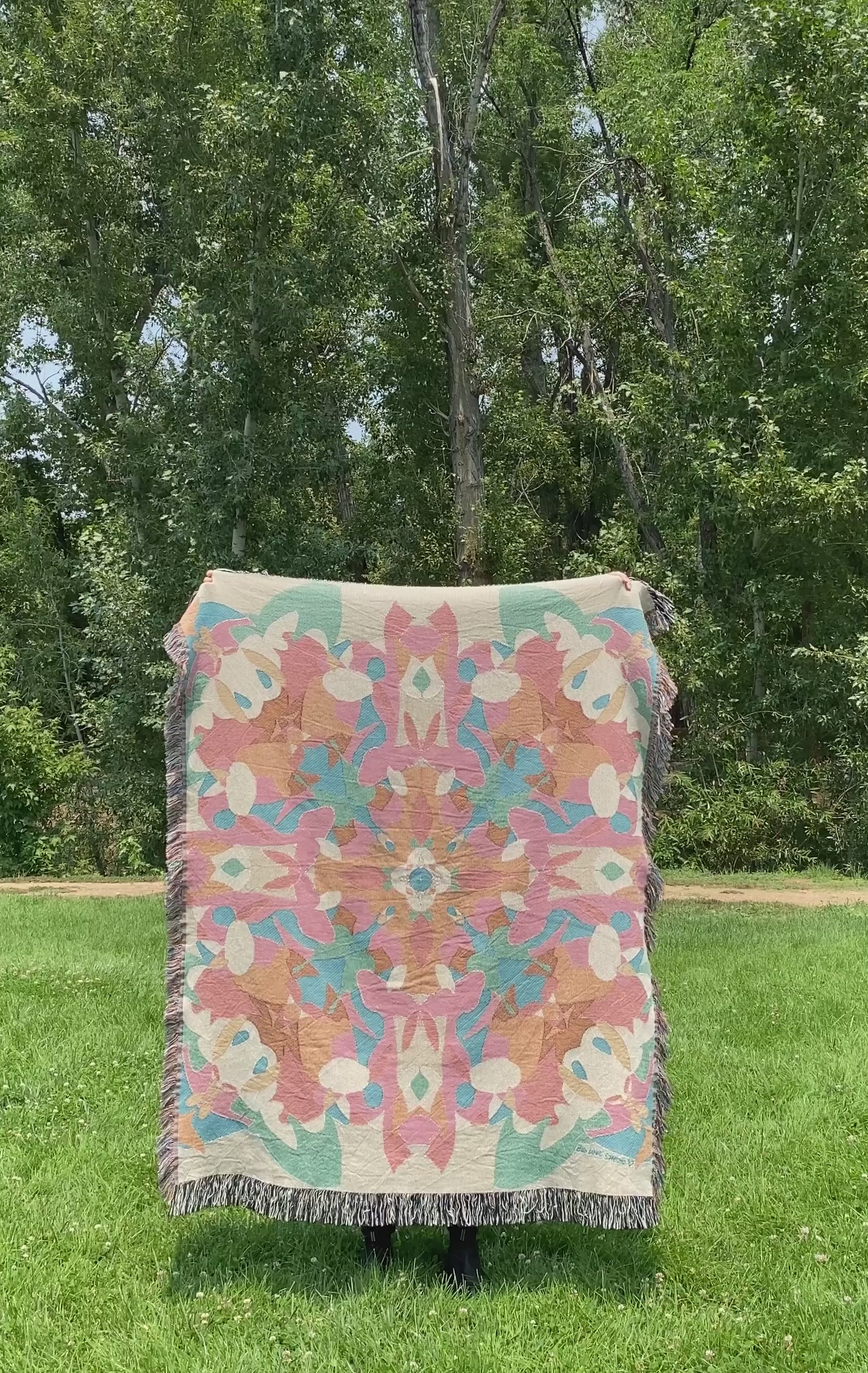Mackenzie flips a brightly colored kaleidoscope woven blanket with fringe to see the front and black