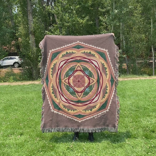 Mackenzie flips a brown and green mandala woven blanket with fringe to see the front and back