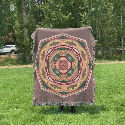 Mackenzie flips a brown and green mandala woven blanket with fringe to see the front and back
