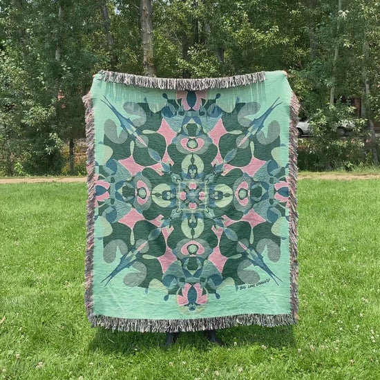 Mackenzie flips a green kaleidoscope woven blanket with fringe to see the front and back