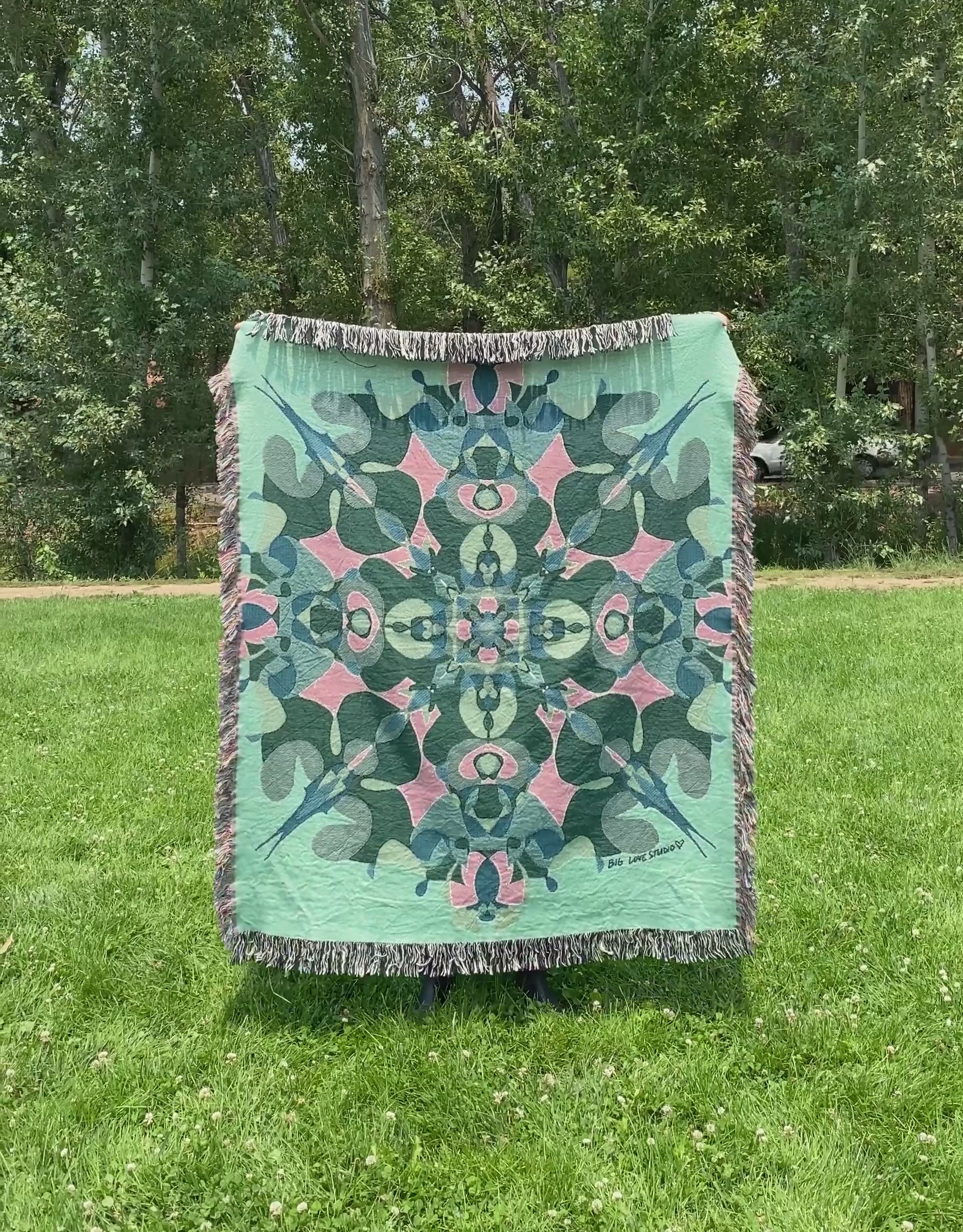 Mackenzie flips a green kaleidoscope woven blanket with fringe to see the front and back