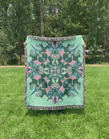 Mackenzie flips a green kaleidoscope woven blanket with fringe to see the front and back