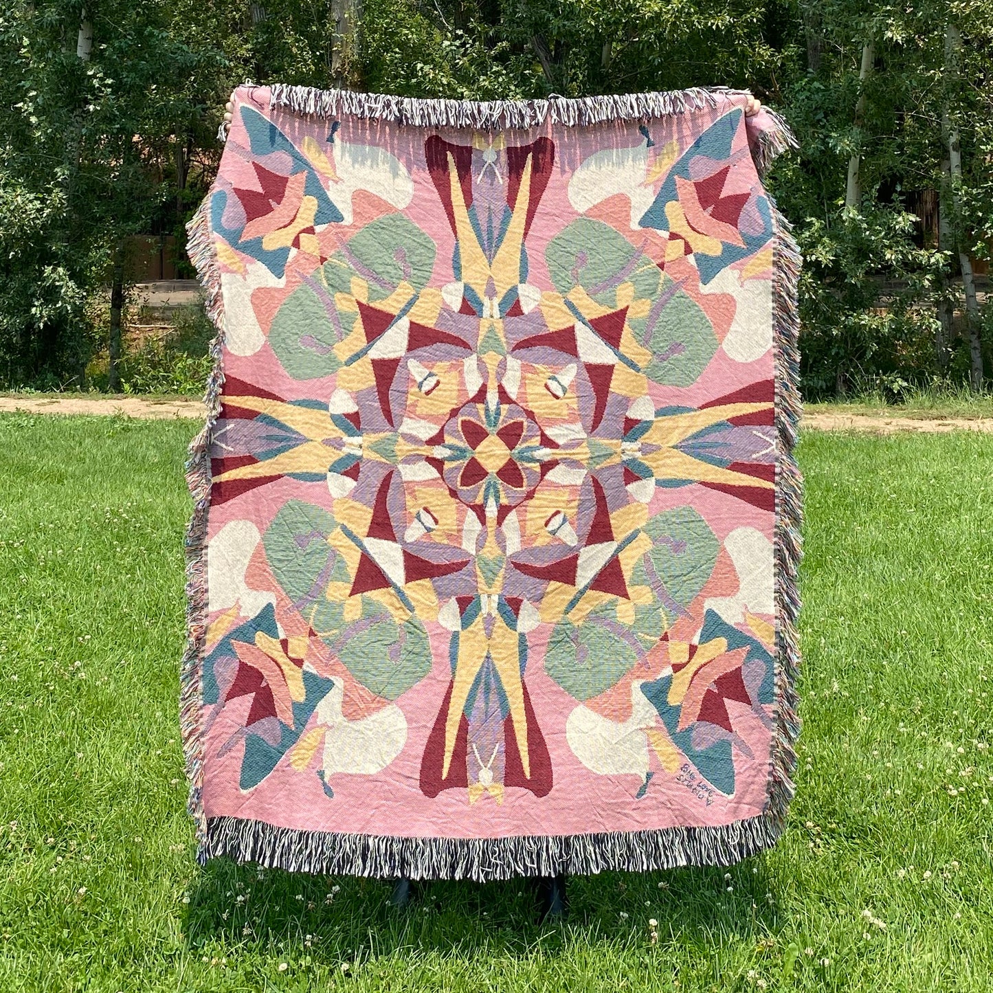 A colorful pink and red patterned kaleidoscope blanket with fringe