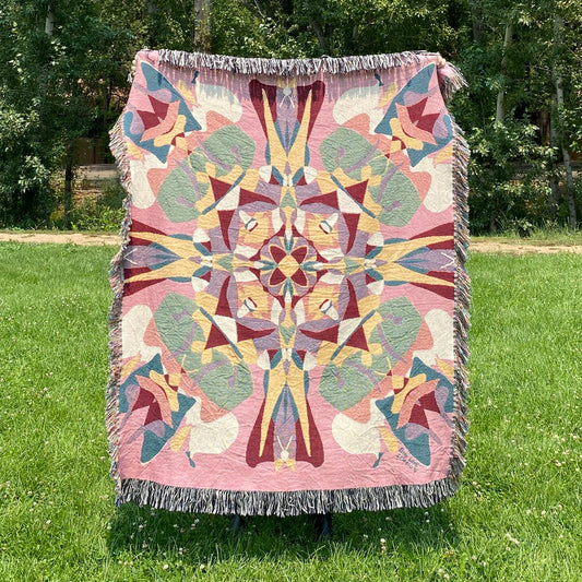 A colorful pink and red patterned kaleidoscope blanket with fringe