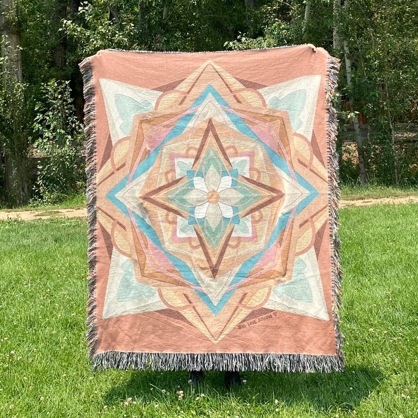 A colorful mandala patterned blanket with fringe in coral and greens