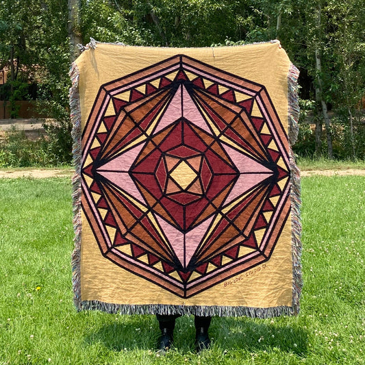 A yellow, oranges, and reds mandala blanket inspired by stained glass with fringe